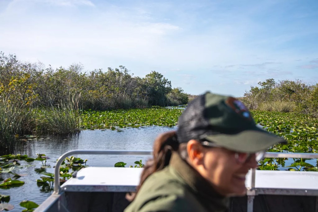 A Park Ranger sits on an airboat on a bright blue day.