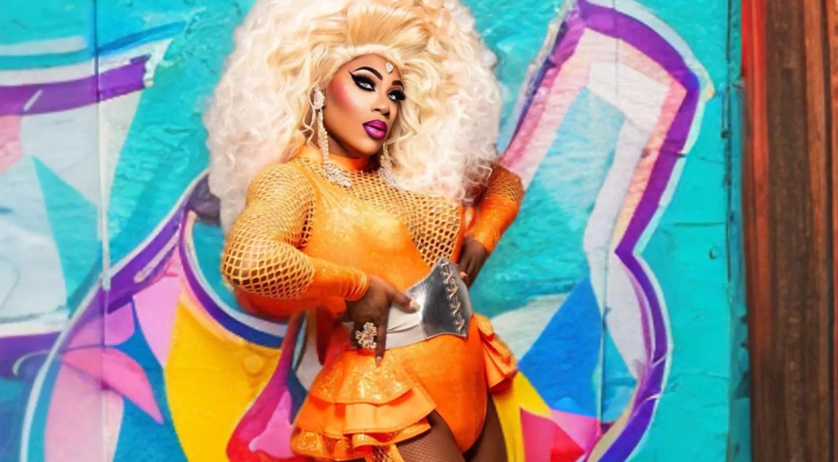 portrait of a drag queen in a blonde wig and orange outfit