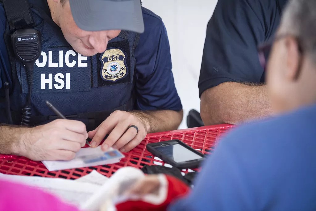 U.S. Immigration and Customs Enforcement officers sit across from a man