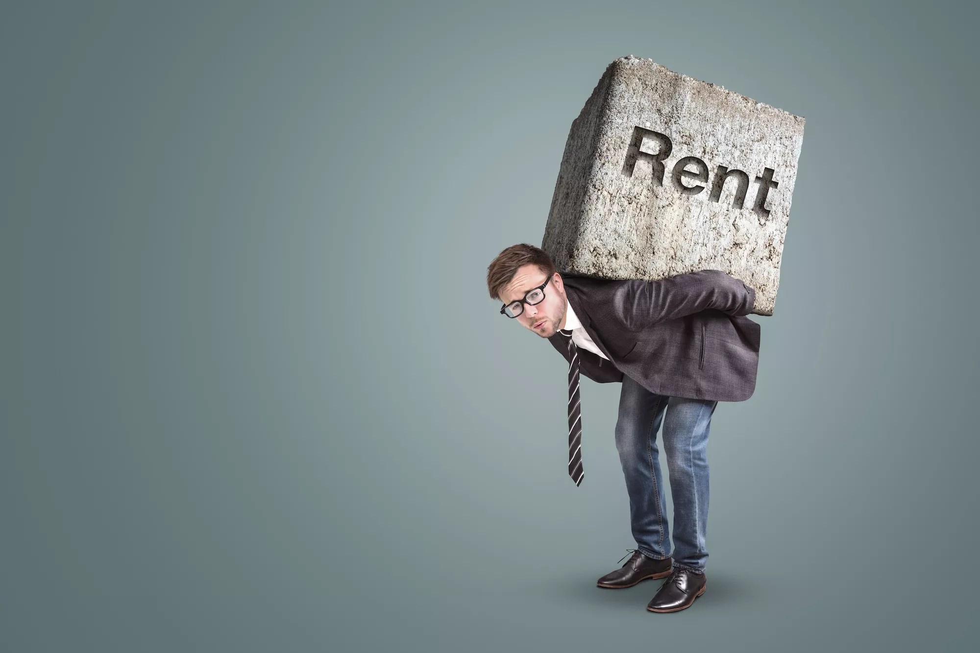 well-dressed hunched man with what looks to be a very heavy concrete block on his back with the word "Rent" etched into it (Conceptual image of a man burdened by high rent)