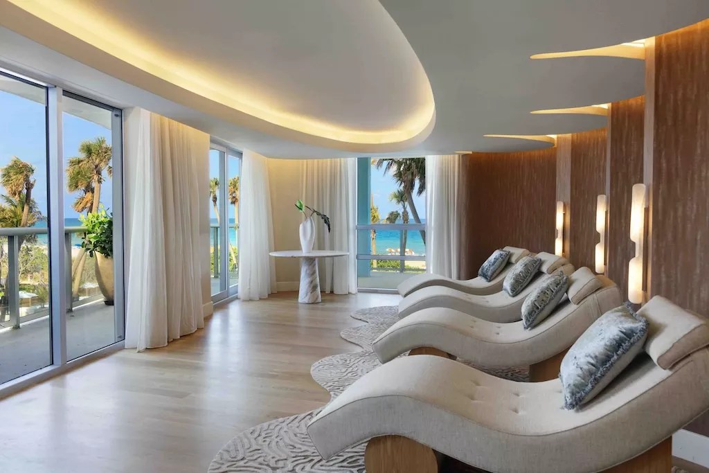 photo of lounge chairs facing windows with palms and the ocean in the distance