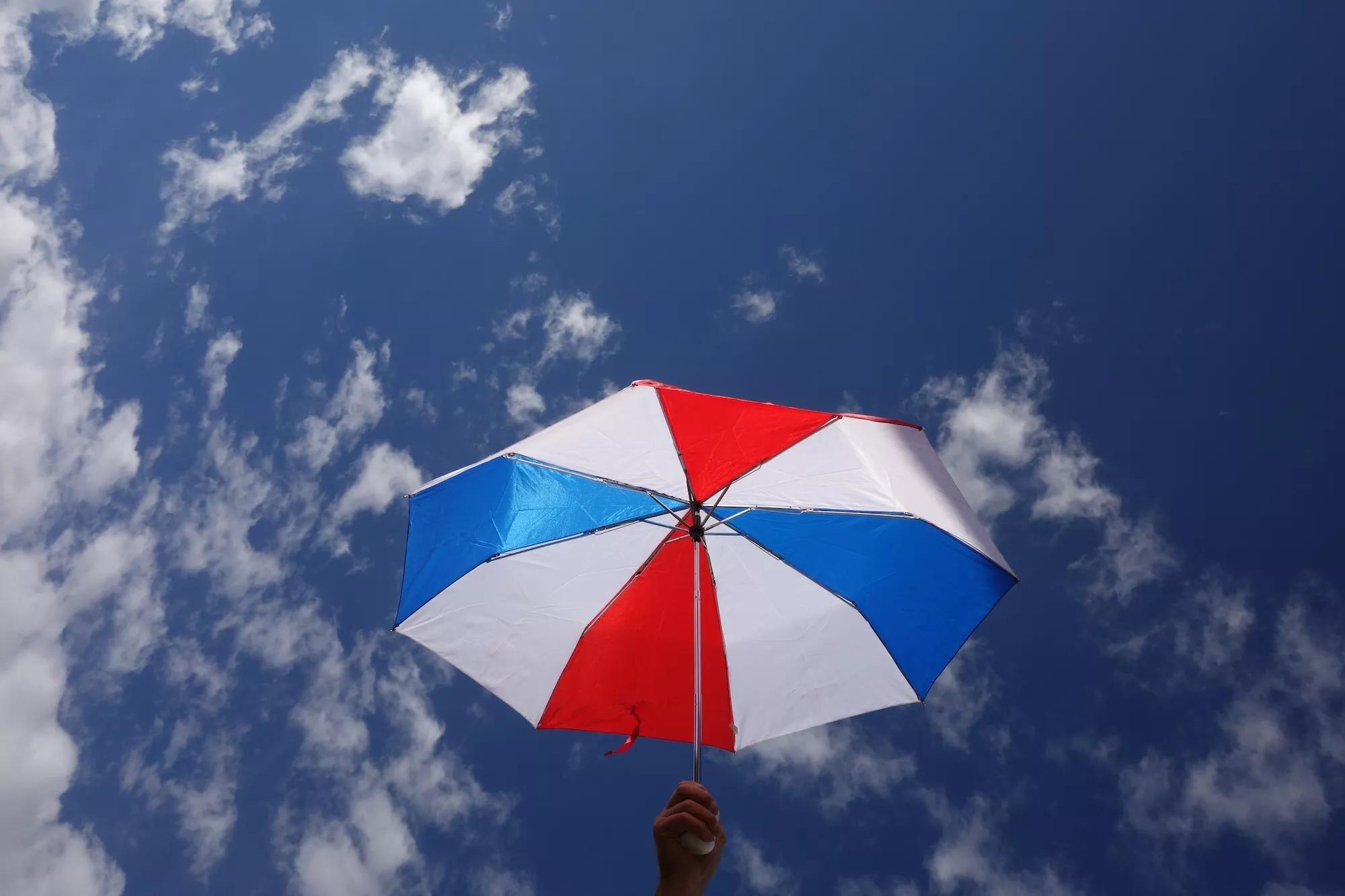A red, white, and blue umbrella held up against a mostly clear sky with scattered clouds
