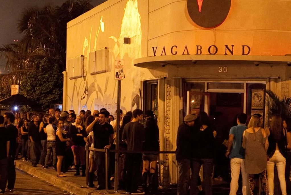 A line of people outside of a venue with a sign that reads Vagabond 
