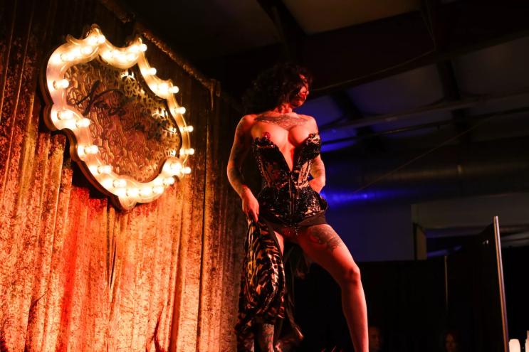 a burlesque dancer lowers a corset to reveal bejeweled tassels on her breasts
