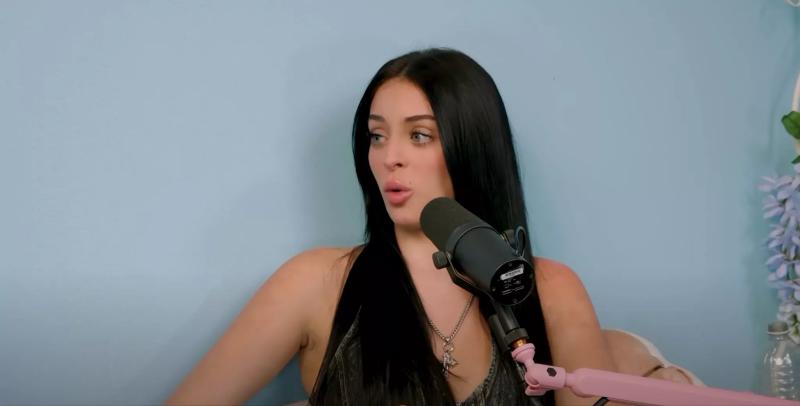 a woman sits in front of a microphone to record a podcast