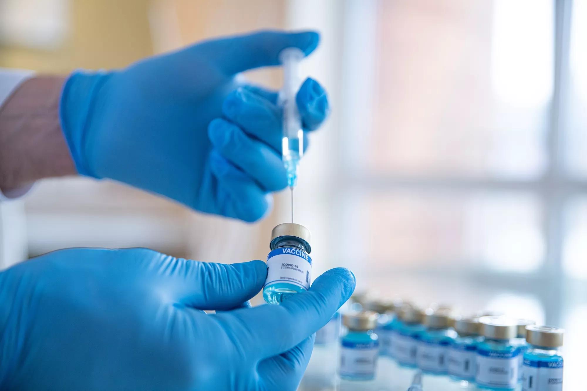 stock photo showing a the hands of a gloved lab worker filling a syringe from an ampule with more ampules in the blurred background