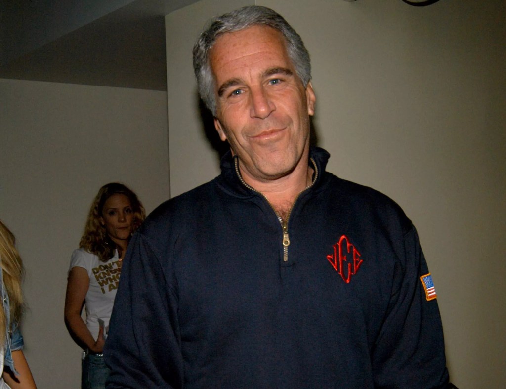 Jeffrey Epstein looking at the camera wearing the blue quarter zip sweatshirt with red monogrammed initials