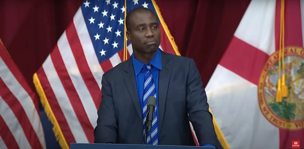 Florida Surgeon General speaking at press conference wearing a blue tie and black jacket