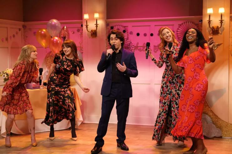 four women surround a man singing at a reception