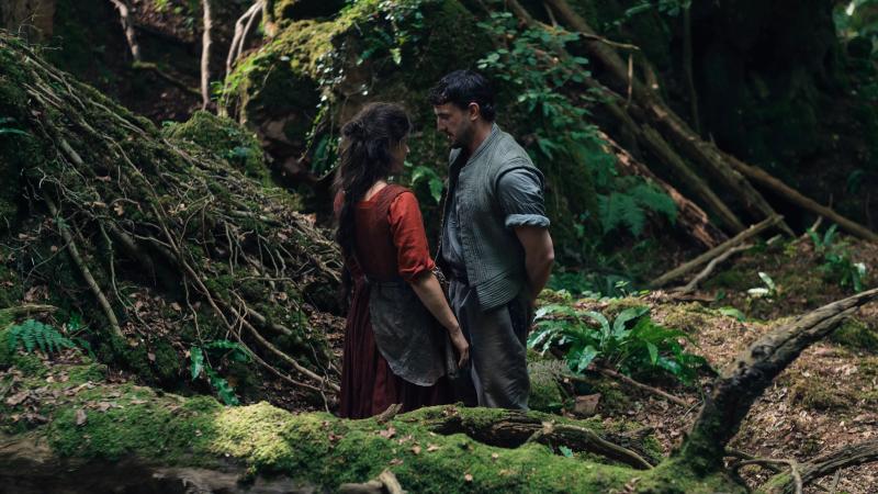 film still of actors Jessie Buckley and Paul Mescal playing the parts of Agnes and William Shakespeare gazing into each other's eyes in the middle of a forest