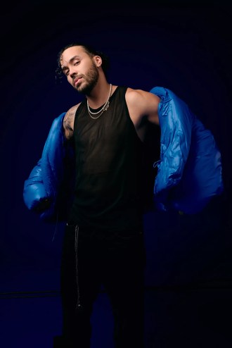 Portrait of a man posing for the camera wearing black pants, a black shirt, and a blue jacket.